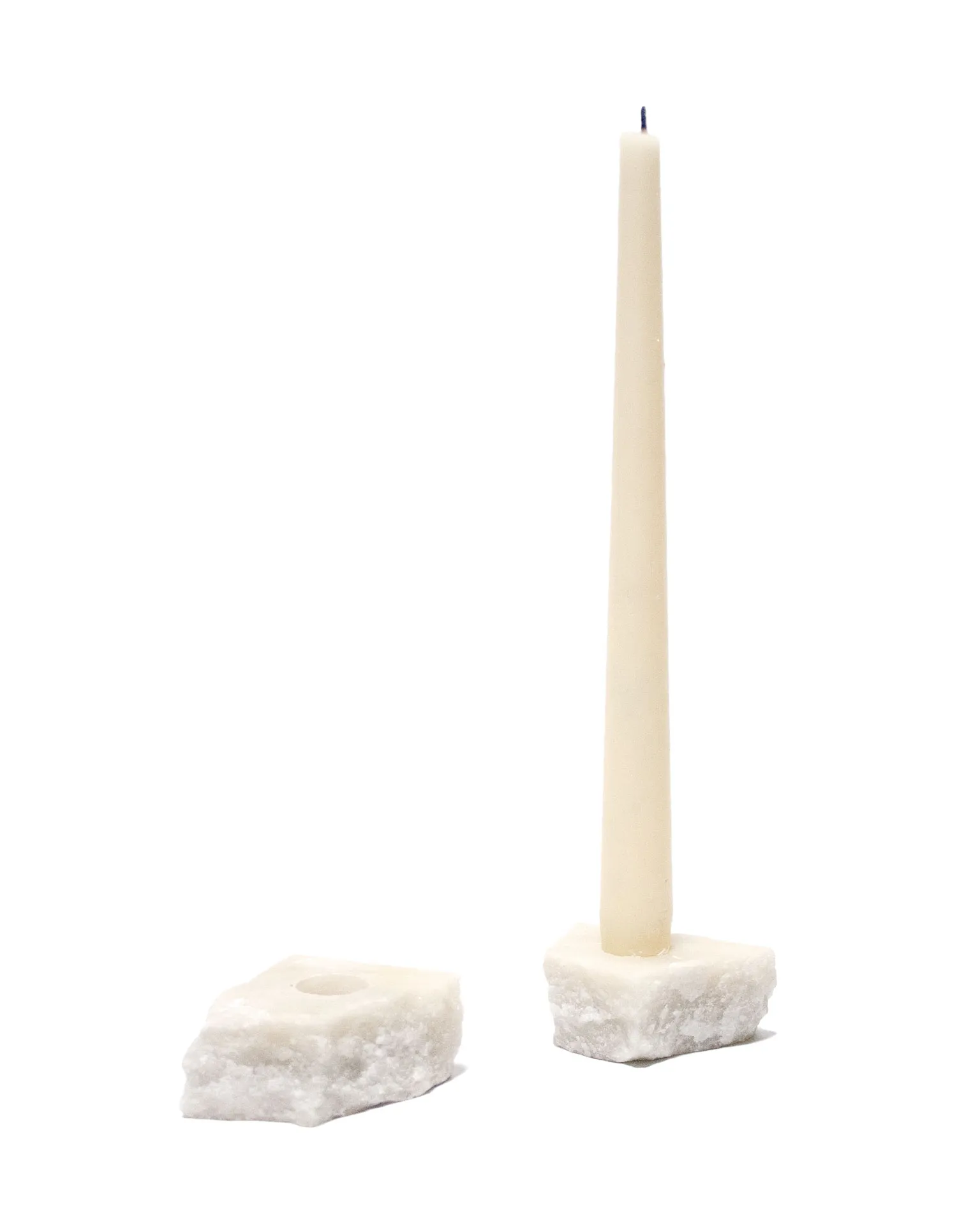 The 'Lithic Candle Holder' created by Jannis Schäfer Studio, made from a reclaimed marble tabletop. The design features a tall, tapered candle held by a square marble base. This upcycled, recycled, and transformed piece is part of a series of derivative designs.