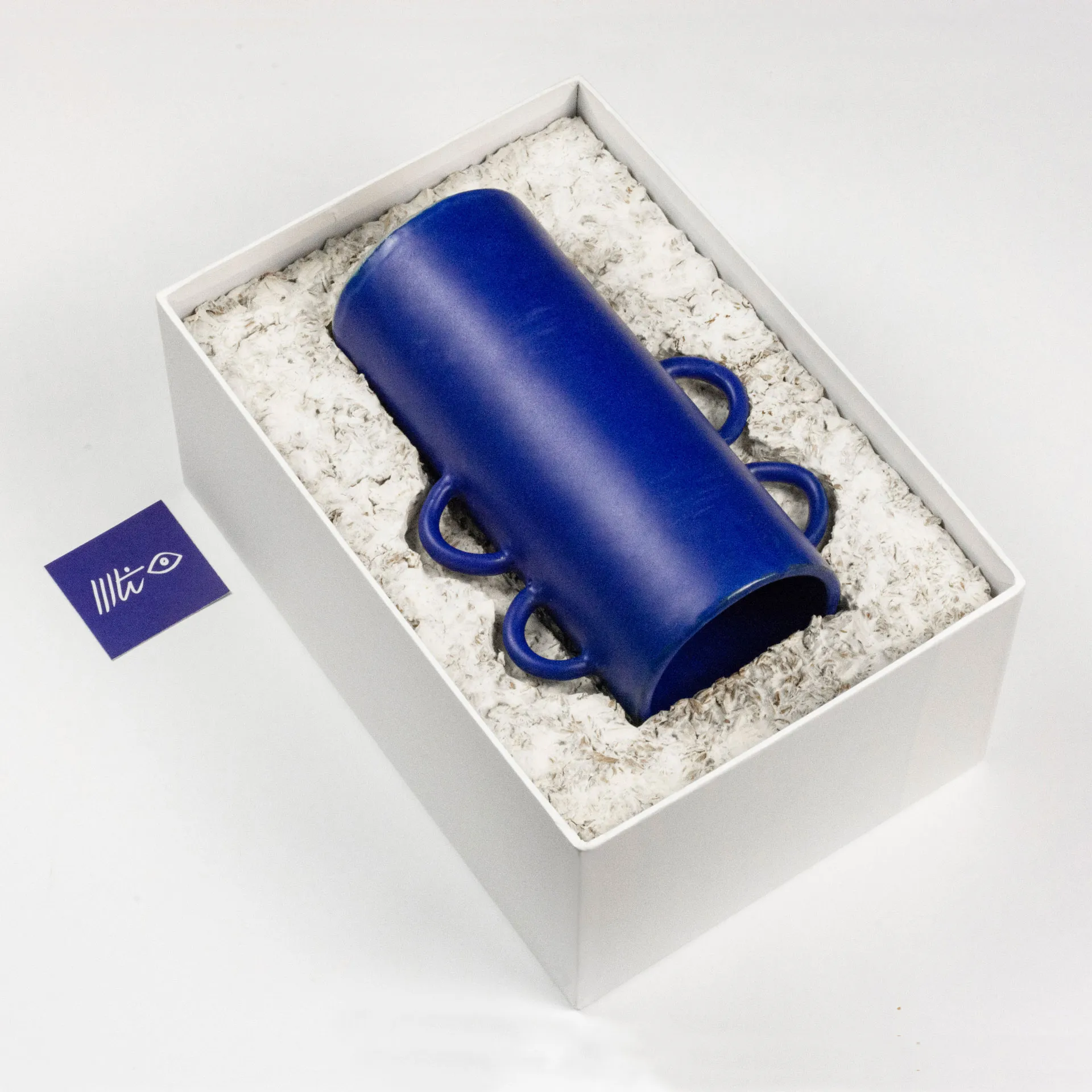 A blue vase designed by cini matilde inside a white box with cushioning material made from mycelium packaging grown on 100% BSG designed by Studio Jannis Schäfer. 