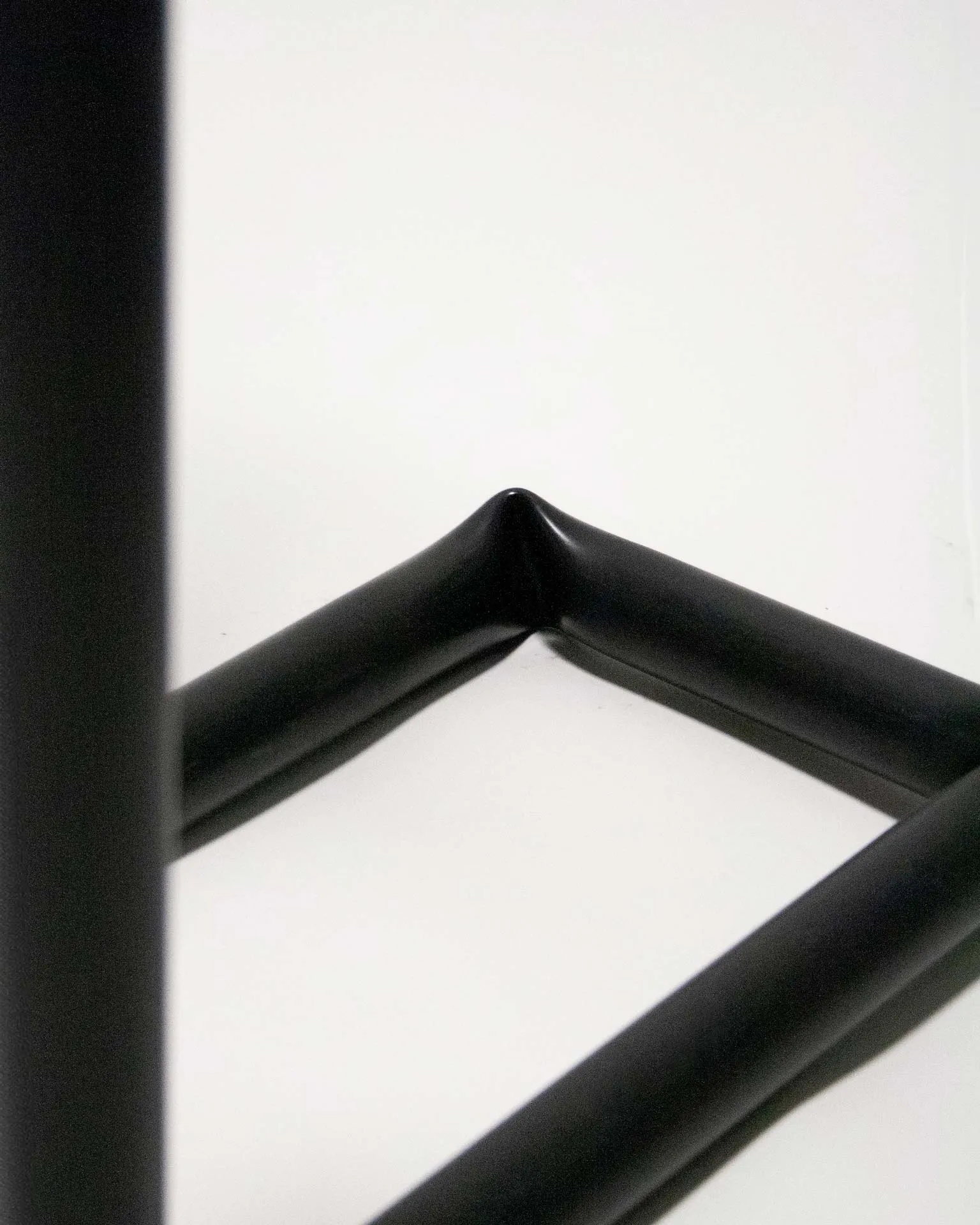 A toilet paper holder created by Jannis Schäfer Studio, made from a reclaimed PVC tube. The design features a black, L-shaped frame with one vertical rod holding a roll of toilet paper at the top and a second vertical rod holding multiple spare rolls. This object is part of a series of upcycled, recycled, and transformed designs.