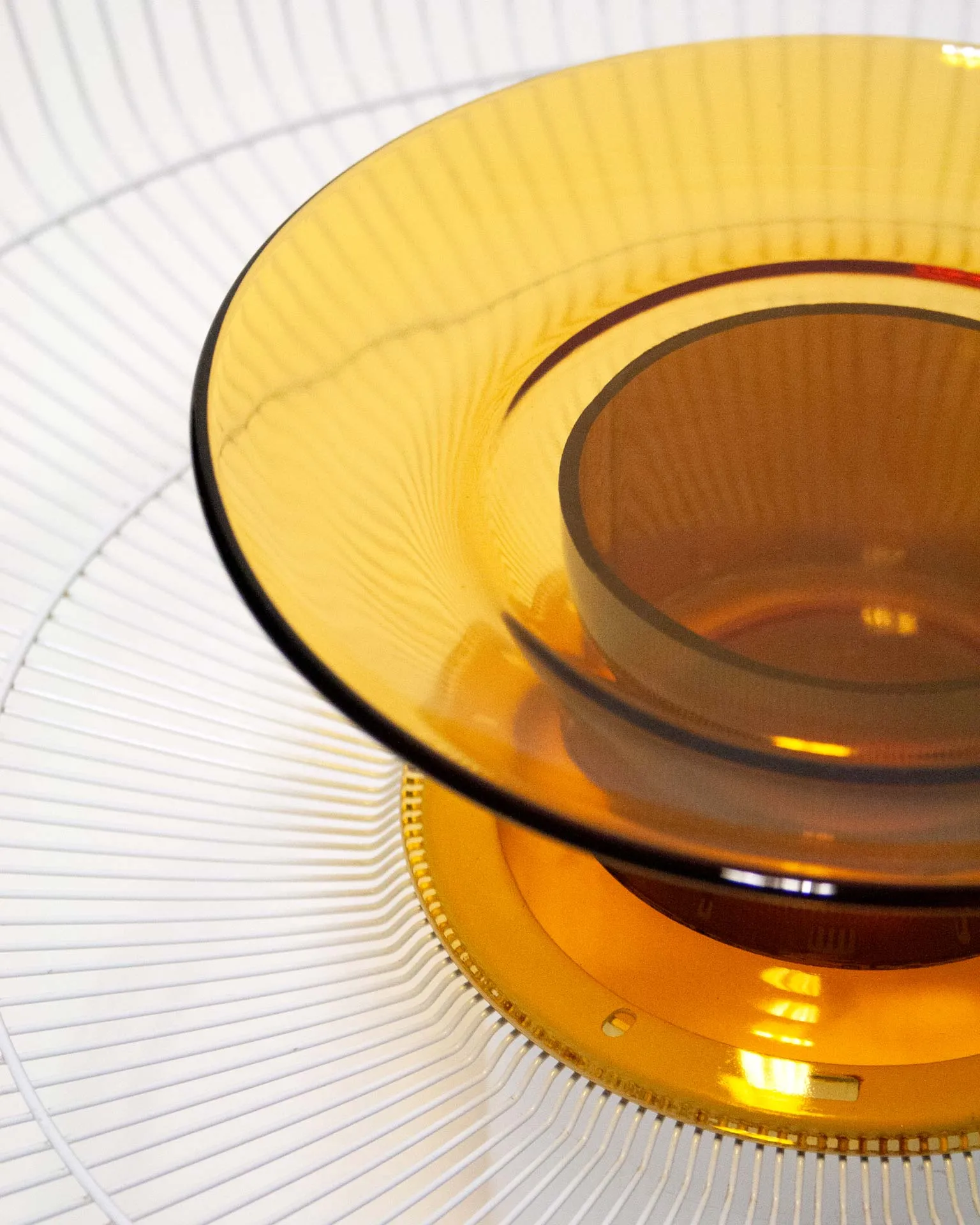 A modern fruit bowl created by Jannis Schäfer Studio, combining upcycled and transformed reclaimed materials. The design features a ventilator shield repurposed into a bowl with concentric wire rings and a central element consisting of a Duralex glass plate and a glass cylinder derived from a bottle. This object is part of a series of derivative designs.