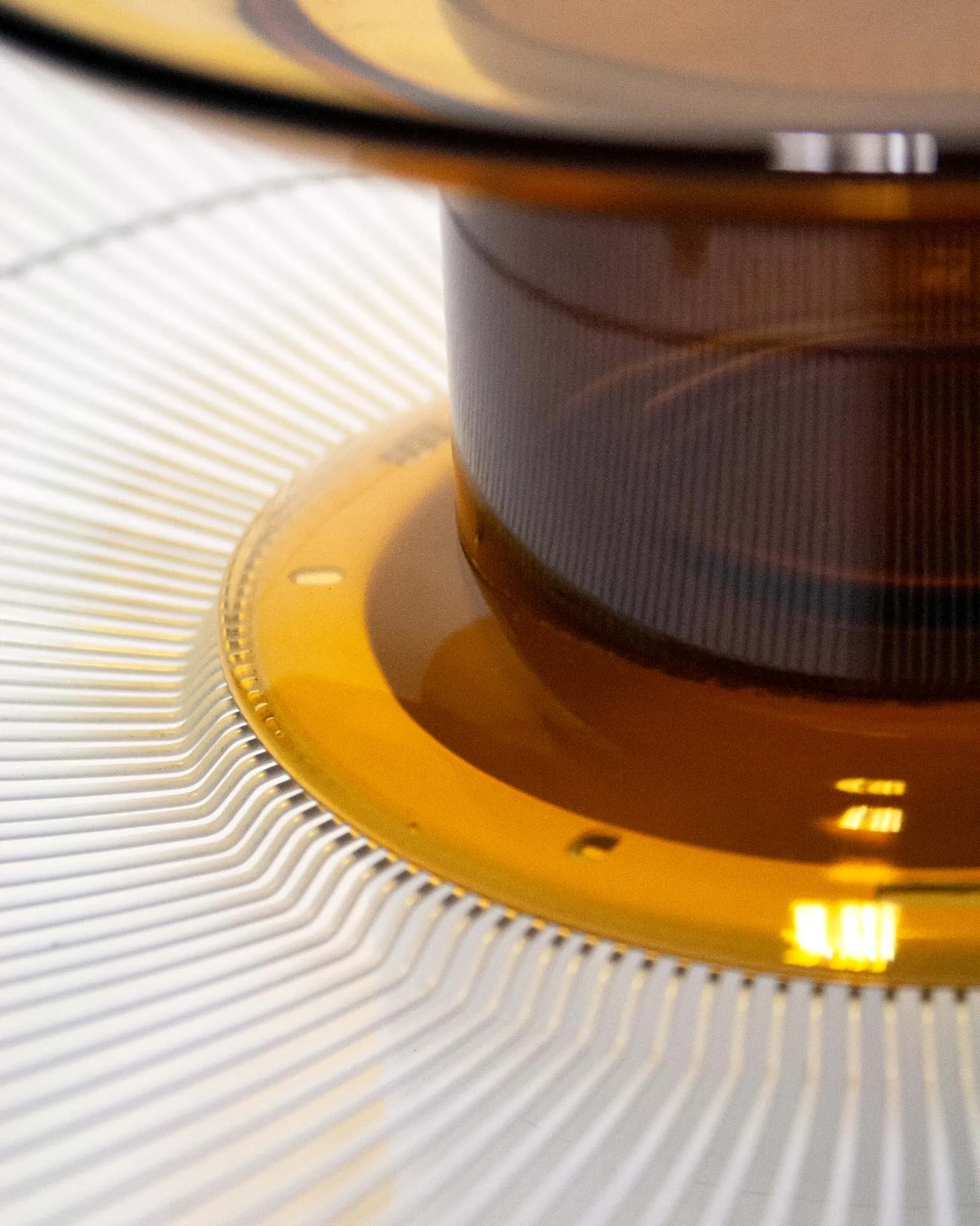 A modern fruit bowl created by Jannis Schäfer Studio, combining upcycled and transformed reclaimed materials. The design features a ventilator shield repurposed into a bowl with concentric wire rings and a central element consisting of a Duralex glass plate and a glass cylinder derived from a bottle. This object is part of a series of derivative designs.