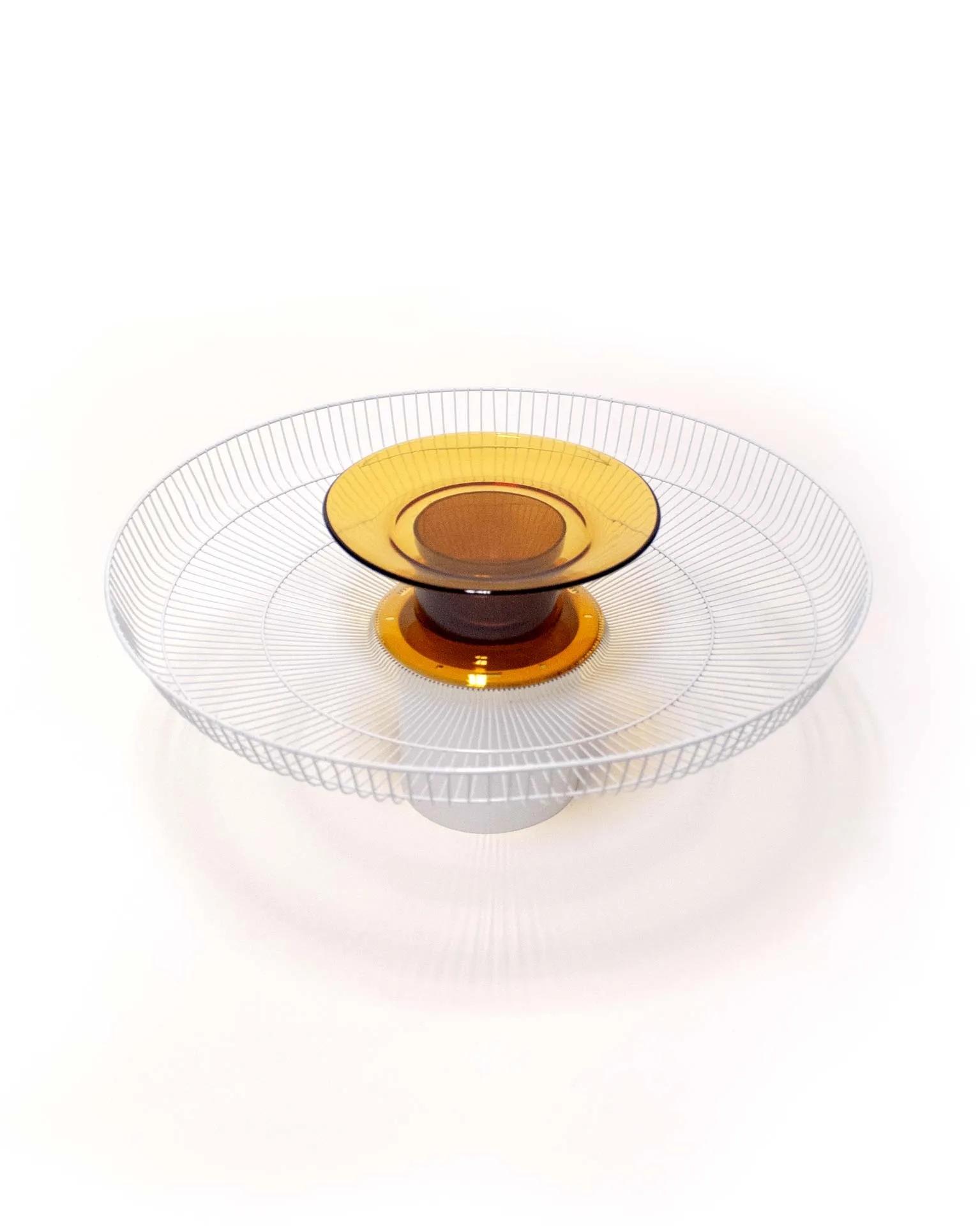 A modern fruit bowl created by Jannis Schäfer Studio, combining upcycled and transformed reclaimed materials. The design features a ventilator shield repurposed into a bowl with concentric wire rings and a central element consisting of a Duralex glass plate and a glass cylinder derived from a bottle. This object is part of a series of derivative designs.