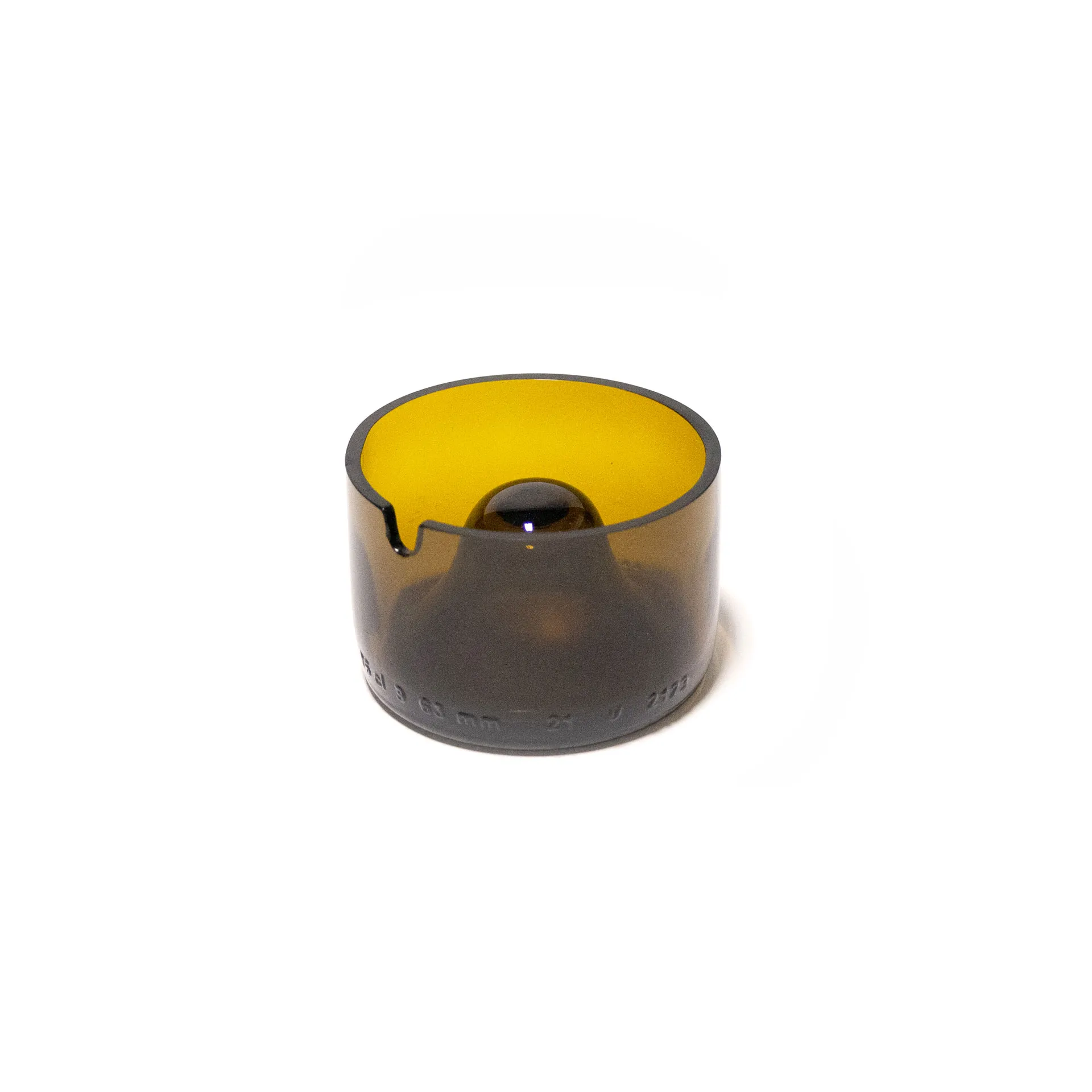 "An amber-colored cylindrical object made from upcycled glass, featuring a central dome and a small notch on the rim. The piece, designed by Jannis Schäfer Studio, is inspired by the Copenhagen ashtray by André Ricard and belongs to a series titled 'Derivatives'. The object highlights the use of reclaimed materials.”