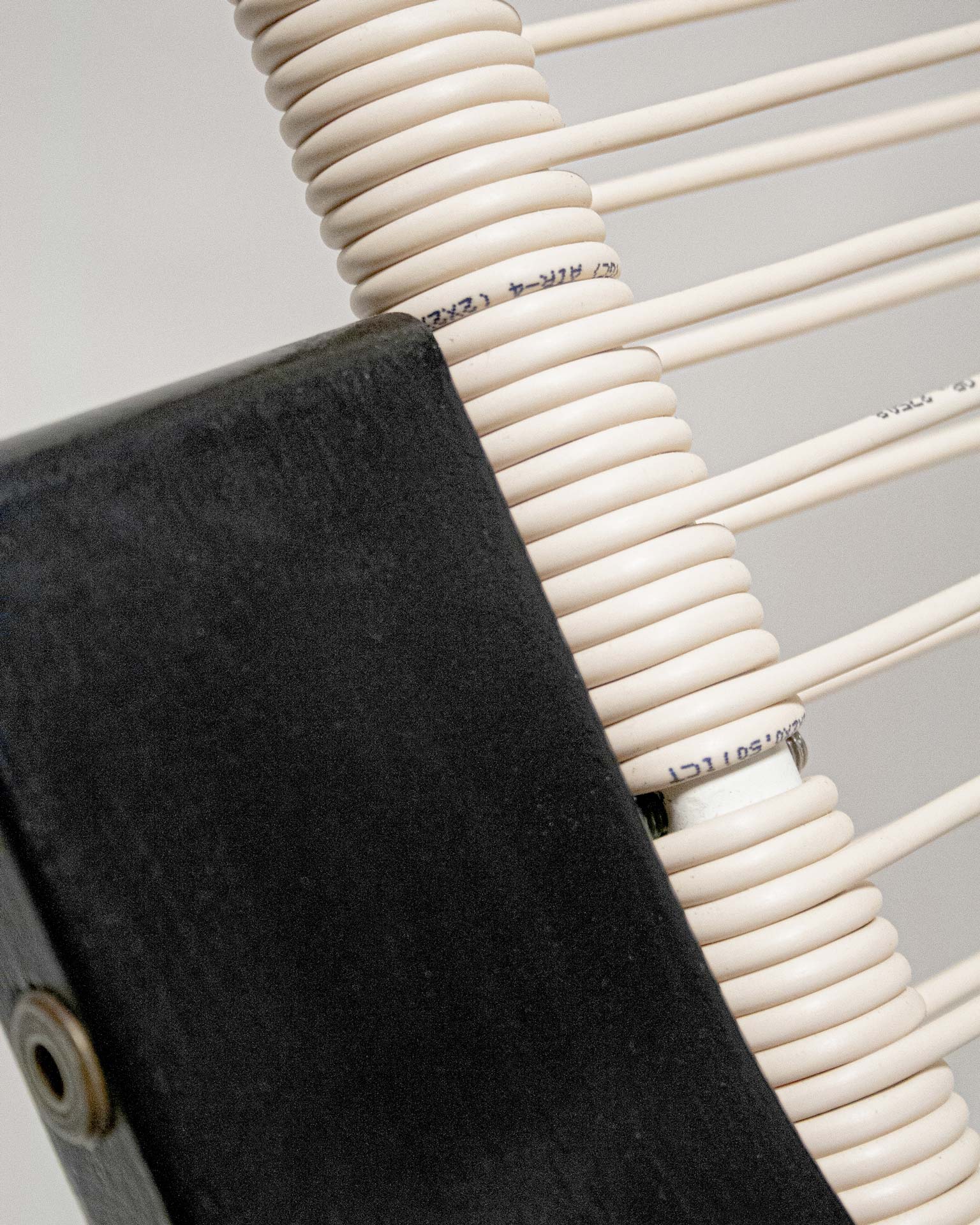 The 'Telefonica Lounge Chair' created by Jannis Schäfer Studio, made from reclaimed telephone cables woven into a supportive seat and backrest. The chair features a sleek black frame with curved armrests and legs. This upcycled, recycled, and transformed piece is part of a series of derivative designs.