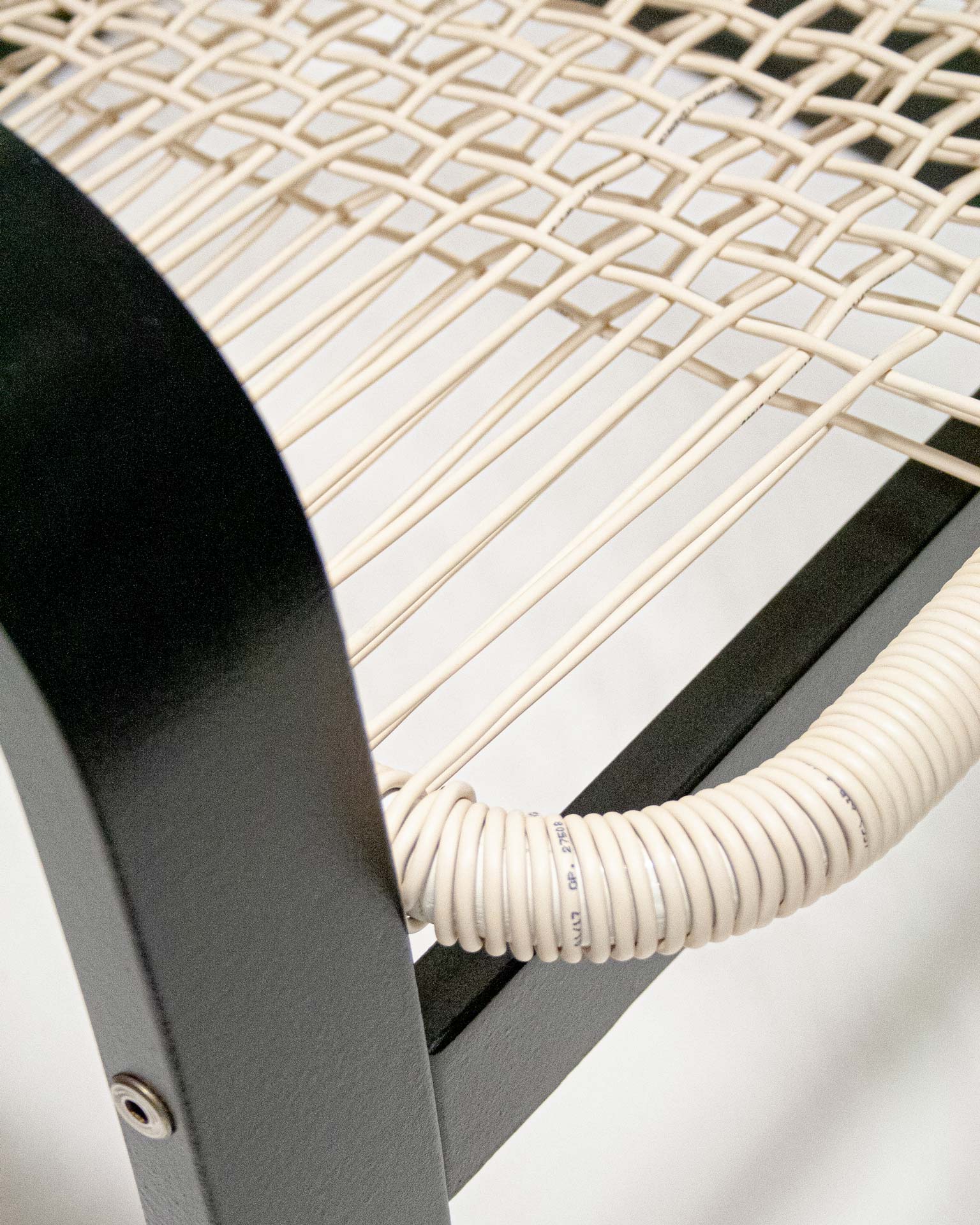 The 'Telefonica Lounge Chair' created by Jannis Schäfer Studio, made from reclaimed telephone cables woven into a supportive seat and backrest. The chair features a sleek black frame with curved armrests and legs. This upcycled, recycled, and transformed piece is part of a series of derivative designs.
