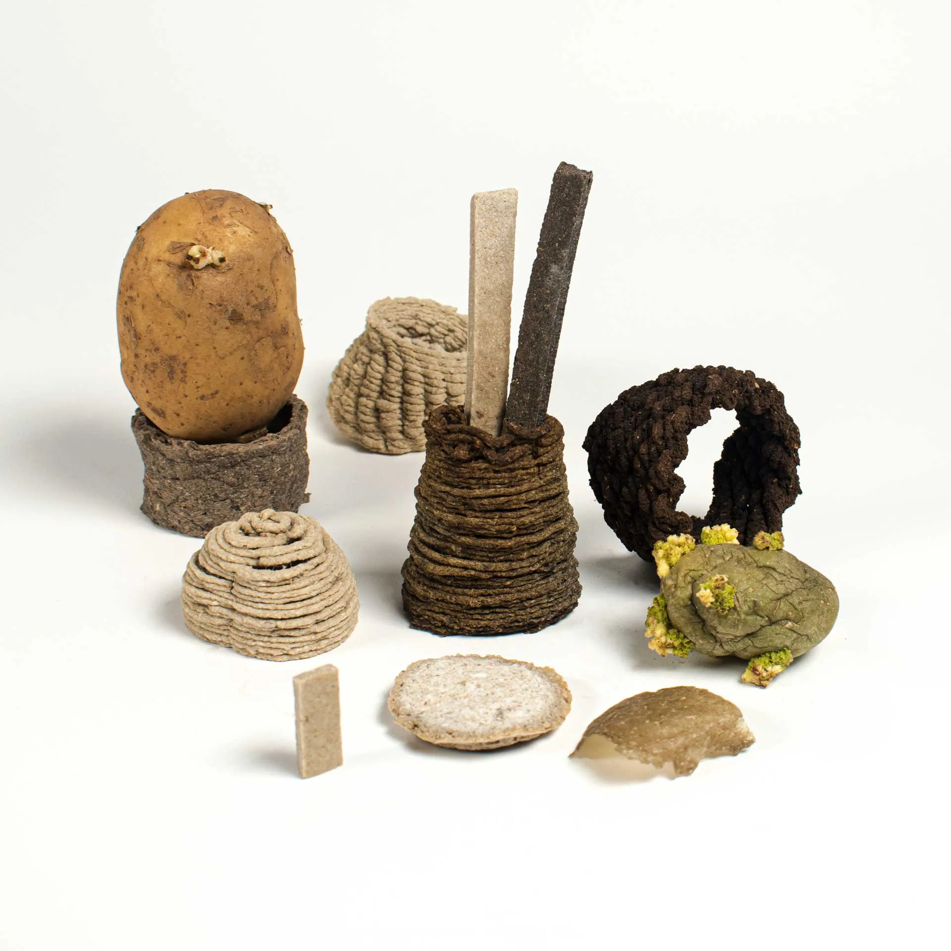 An overview of different manufactured biomaterials created by Jannis Schäfer Studio, titled 'The Nature of Transformation: Lessons from a Potato.' The image showcases various forms made from 100% potato using techniques such as fermentation, 3D printing, hand forming, and molding. The pieces vary in shape and texture, demonstrating the versatility and transformation of potato-based biomaterials.