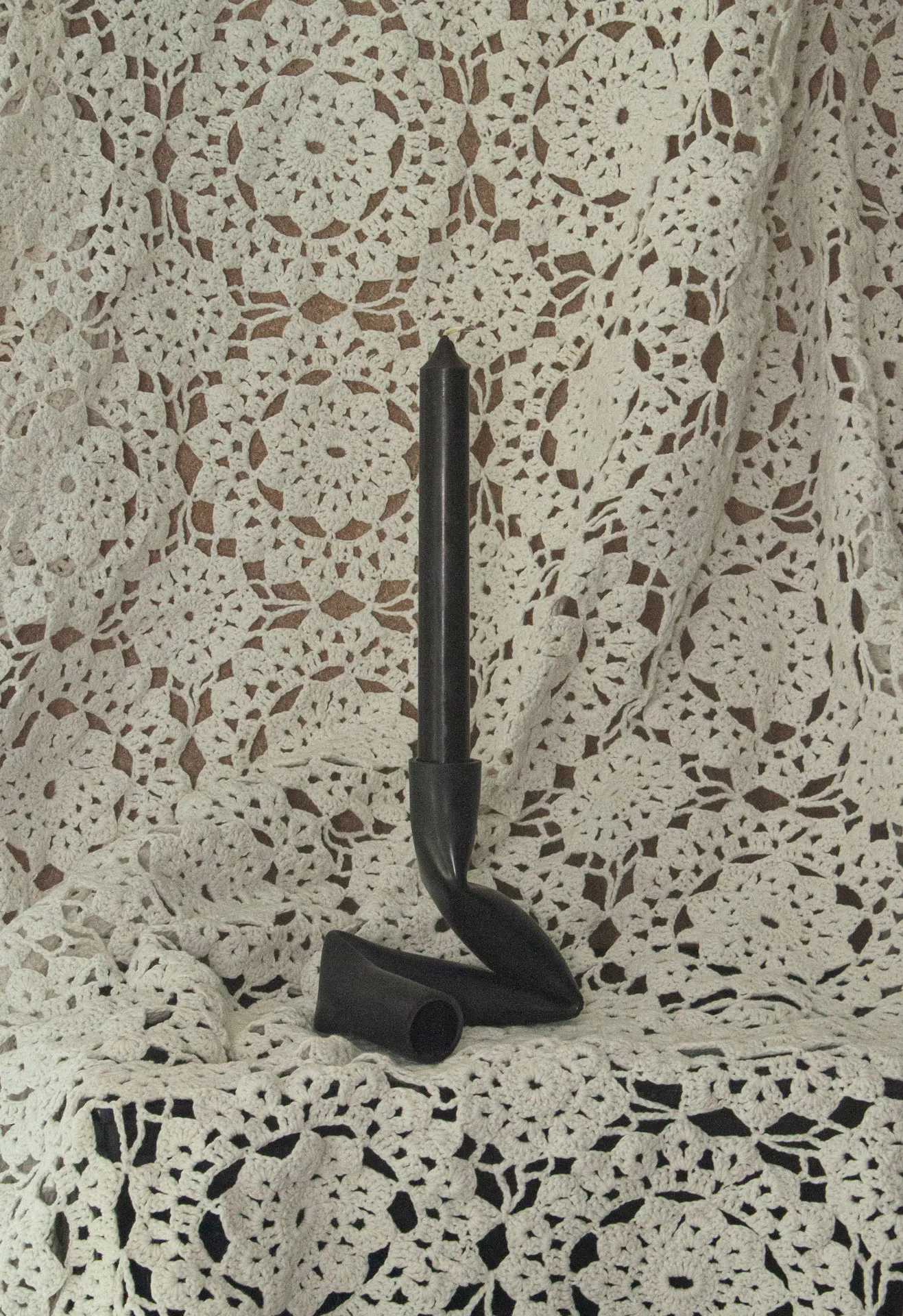 A candle holder created by Jannis Schäfer Studio, made from upcycled PVC tube. The design features a unique, twisted form with two cylindrical openings for candles. This transformed and reclaimed material piece is part of a series of derivative designs.