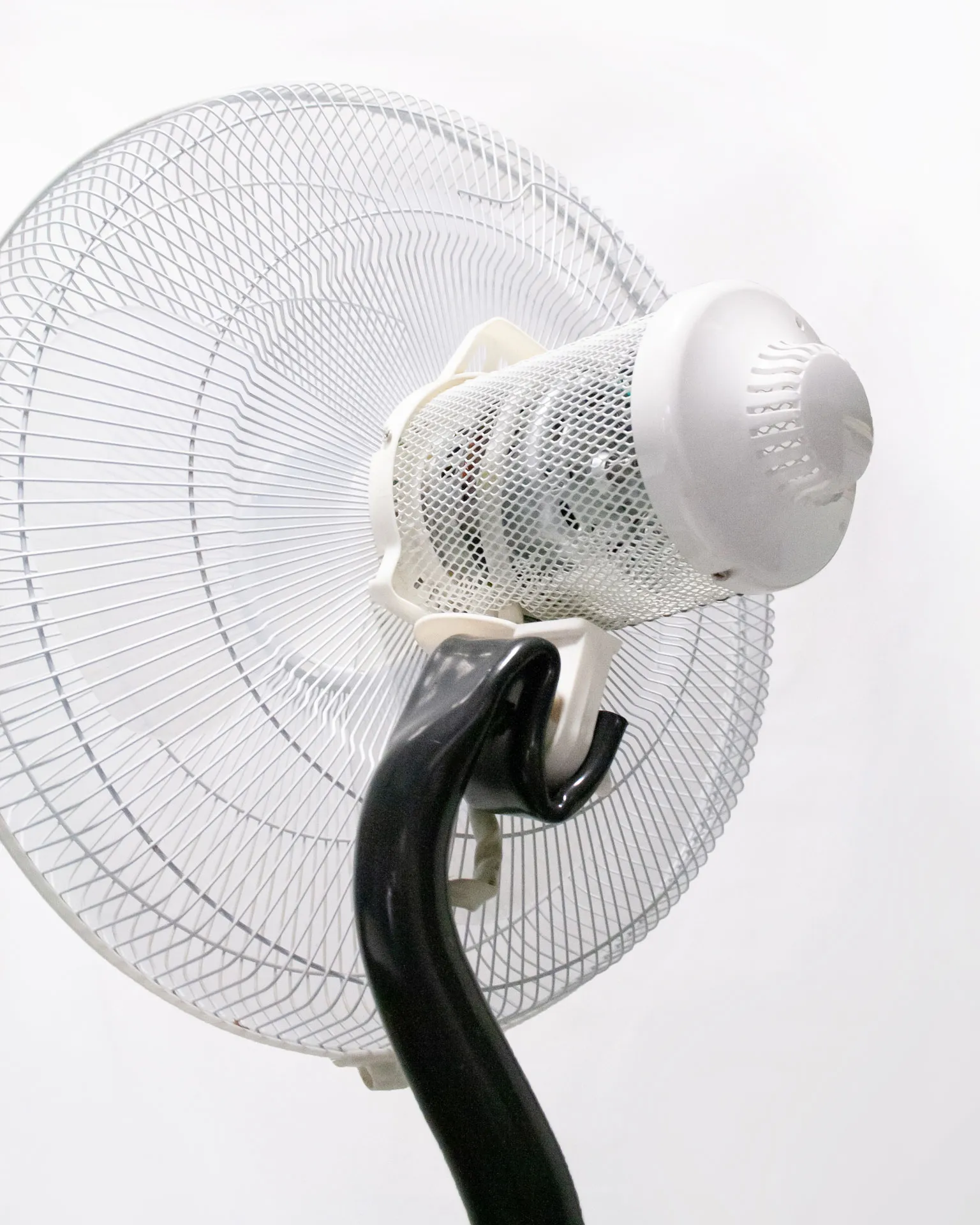 The 'Bent Pipe Blower,' created by Jannis Schäfer Studio, is a ventilator sculpture made from a reclaimed PVC tube and Precious Plastic samples as knobs and buttons. The design features a standing fan with a curved black pipe as the stand, a white circular base, and a clear fan head. This upcycled, recycled, and transformed piece is part of a series of derivative designs.