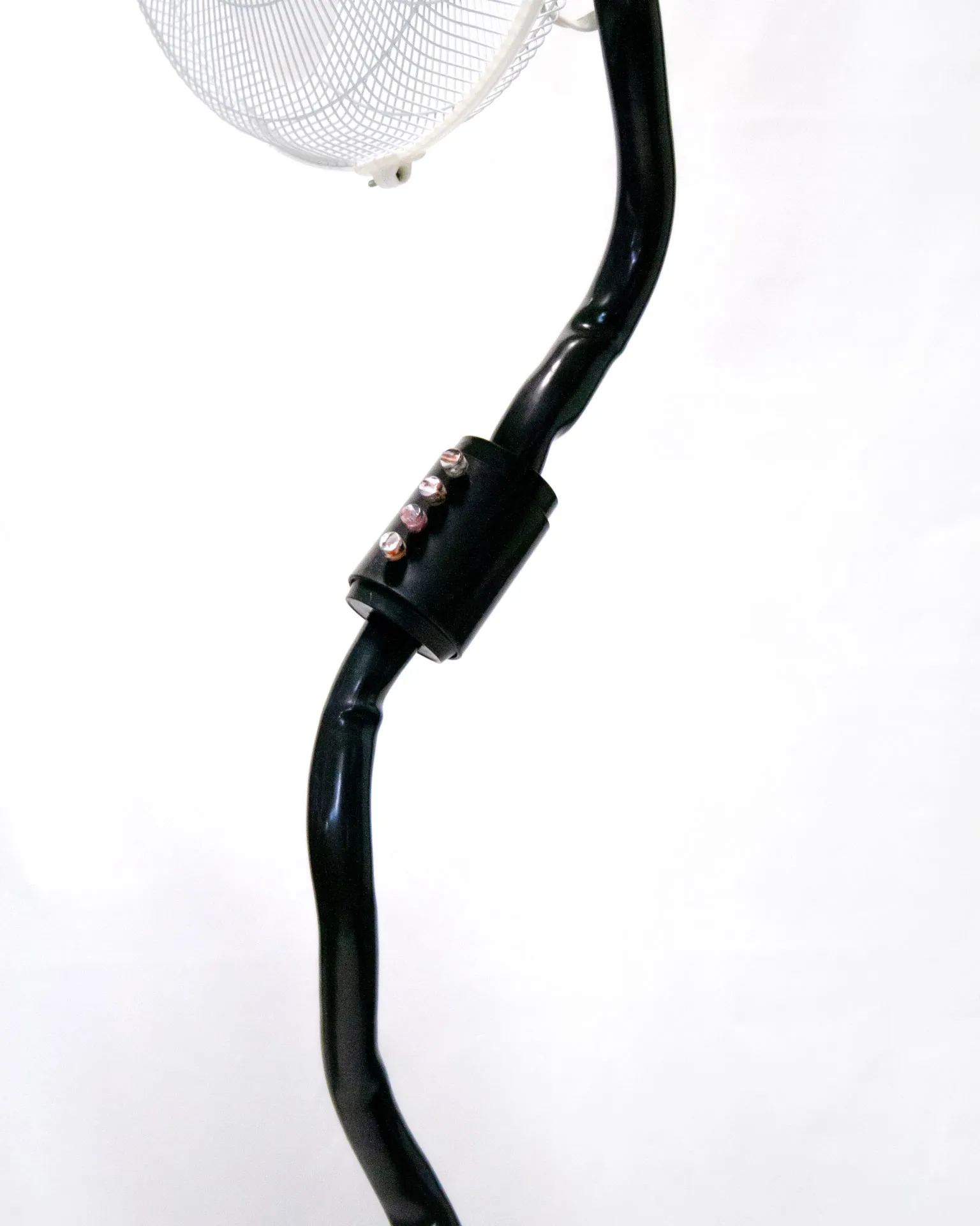 The 'Bent Pipe Blower,' created by Jannis Schäfer Studio, is a ventilator sculpture made from a reclaimed PVC tube and Precious Plastic samples as knobs and buttons. The design features a standing fan with a curved black pipe as the stand, a white circular base, and a clear fan head. This upcycled, recycled, and transformed piece is part of a series of derivative designs.