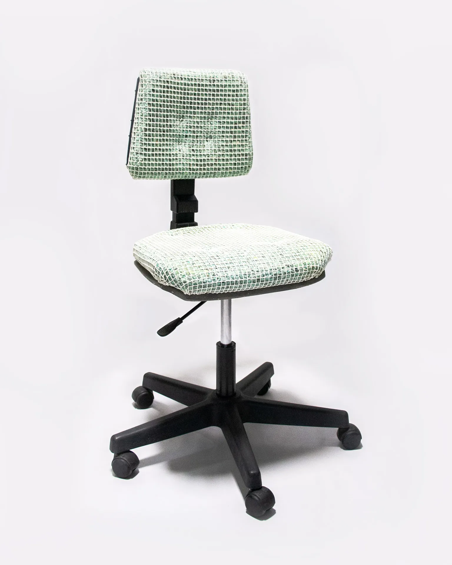 The 'Apollo Office Chair,' created by Studio Jannis Schäfer, is made from recycled insulation material, a plastic grid, and a smoke detector. The design features a cushioned seat and backrest covered in a green and white grid pattern, supported by a black five-wheel base with adjustable height. This upcycled, recycled, and transformed piece is part of a series of derivative designs.