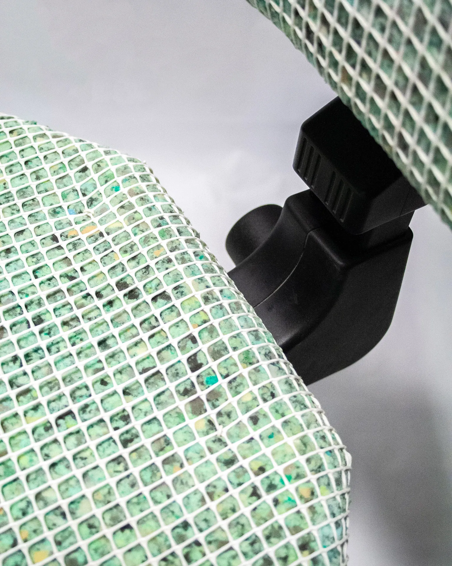The 'Apollo Office Chair,' created by Studio Jannis Schäfer, is made from recycled insulation material, a plastic grid, and a smoke detector. The design features a cushioned seat and backrest covered in a green and white grid pattern, supported by a black five-wheel base with adjustable height. This upcycled, recycled, and transformed piece is part of a series of derivative designs.