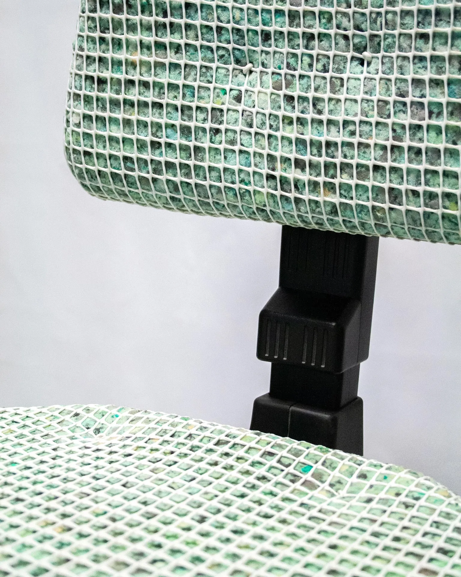 The 'Apollo Office Chair,' created by Studio Jannis Schäfer, is made from recycled insulation material, a plastic grid, and a smoke detector. The design features a cushioned seat and backrest covered in a green and white grid pattern, supported by a black five-wheel base with adjustable height. This upcycled, recycled, and transformed piece is part of a series of derivative designs.