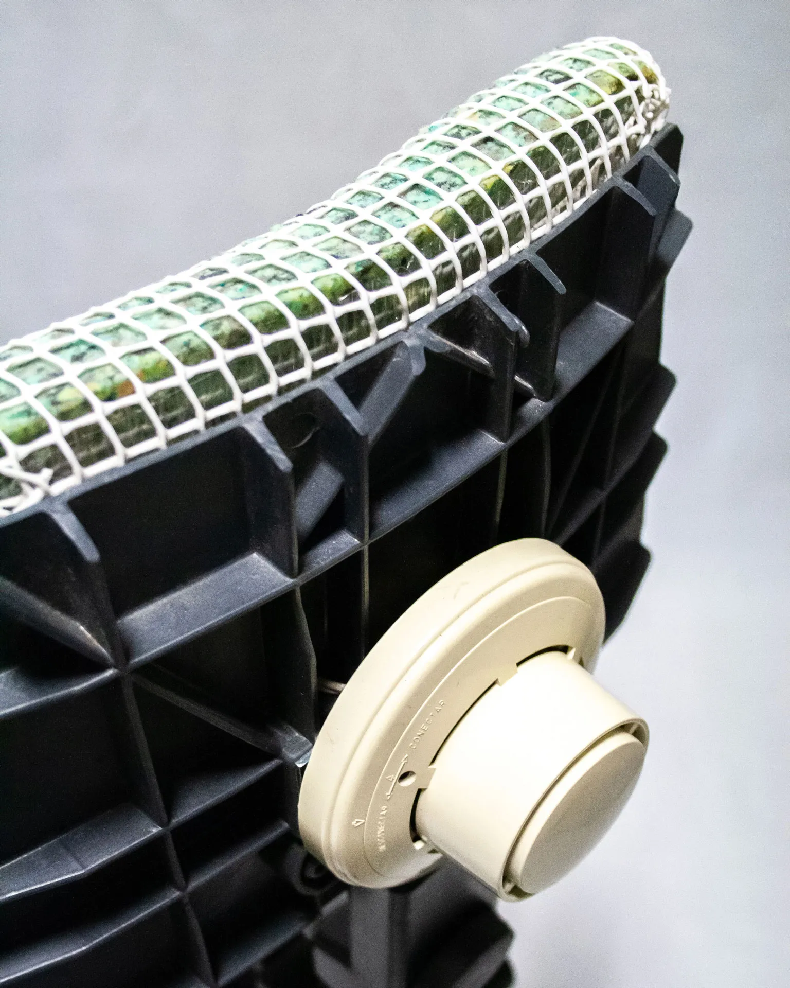 The 'Apollo Office Chair,' created by Studio Jannis Schäfer, is made from recycled insulation material, a plastic grid, and a smoke detector. The design features a cushioned seat and backrest covered in a green and white grid pattern, supported by a black five-wheel base with adjustable height. This upcycled, recycled, and transformed piece is part of a series of derivative designs.