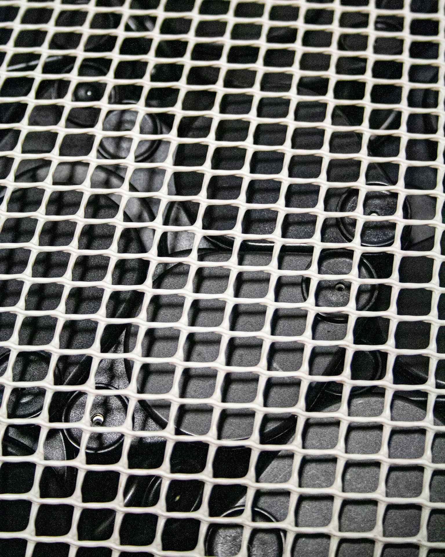 The 'Pinch Bag,' created by Studio Jannis Schäfer, is a pouf made from reclaimed anti-theft labels and a plastic grid. The design features a rectangular shape with a visible grid pattern overlaying the dark material inside. This upcycled, recycled, and transformed piece is part of a series of derivative designs.
