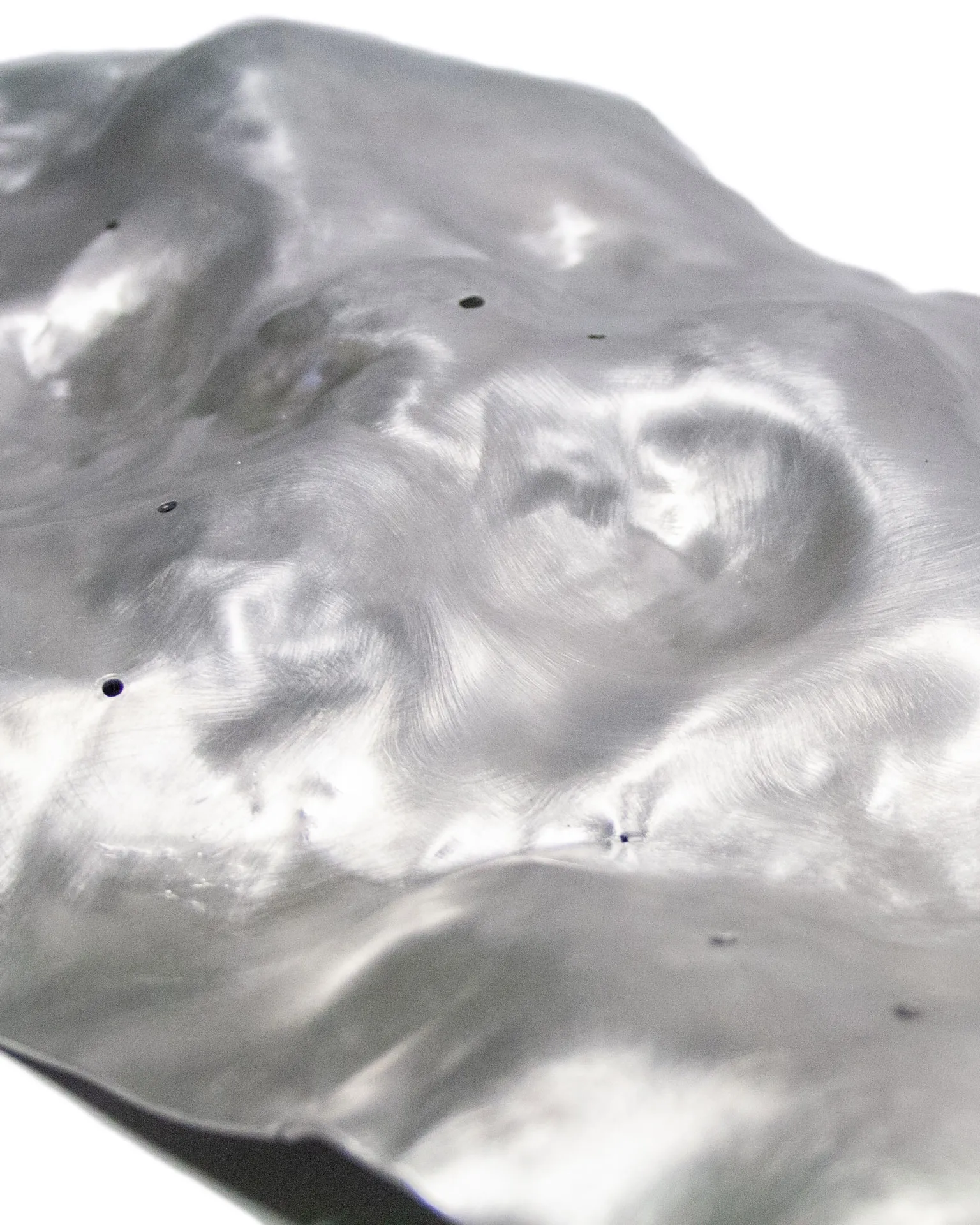 The 'Silver Platter,' created by Jannis Schäfer Studio, is made from a reclaimed aluminum motherboard tray. The design features a textured, undulating surface with a metallic finish. This upcycled, recycled, and transformed piece is part of a series of derivative designs.