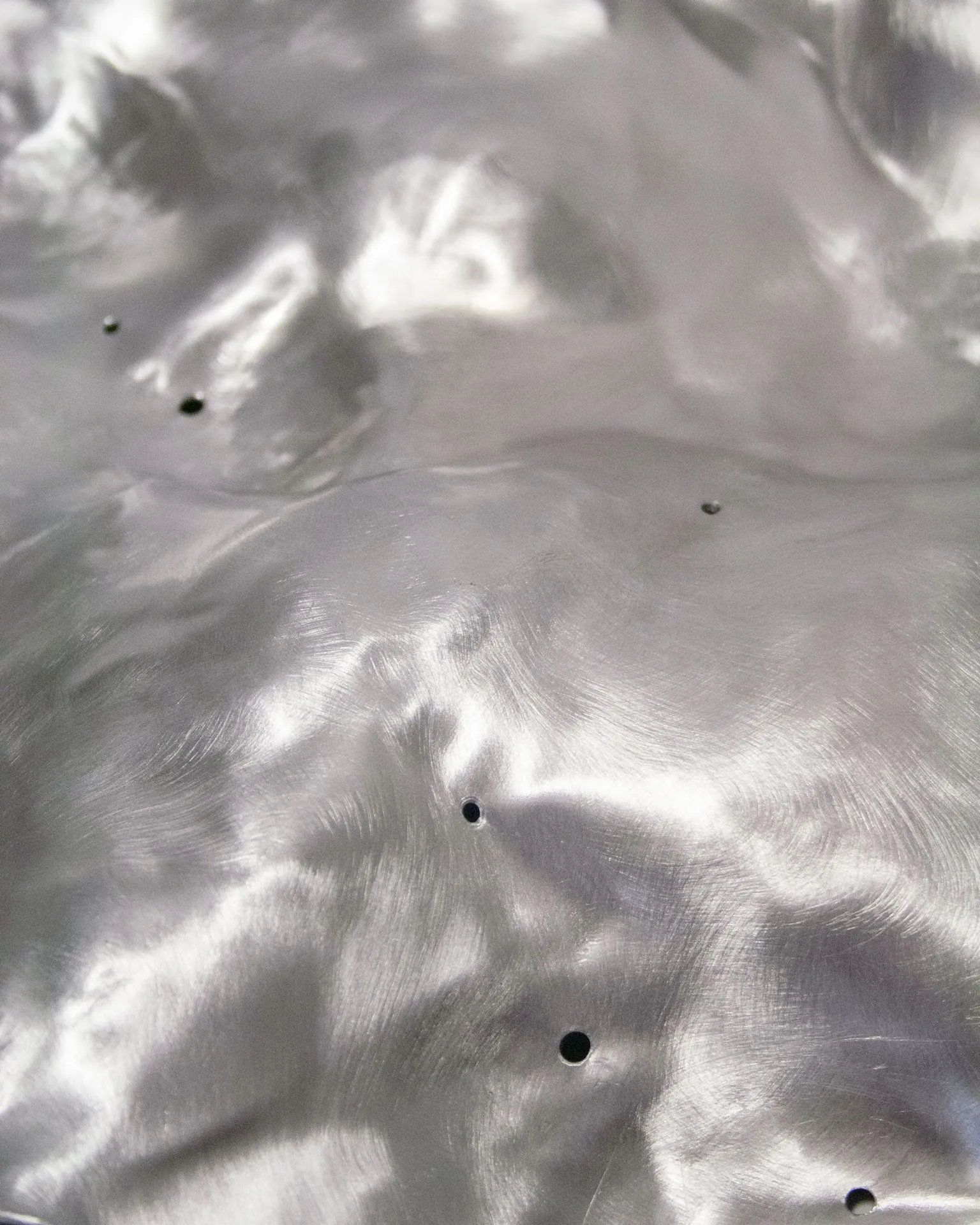 The 'Silver Platter,' created by Jannis Schäfer Studio, is made from a reclaimed aluminum motherboard tray. The design features a textured, undulating surface with a metallic finish. This upcycled, recycled, and transformed piece is part of a series of derivative designs.